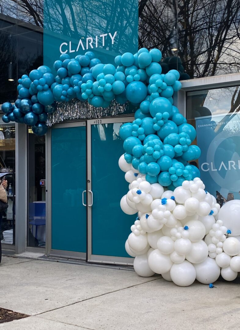 Door to fitness studio festooned with teal and white balloons.