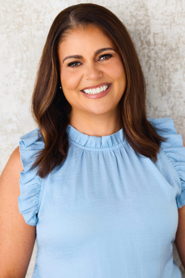 Smiling woman in a light blue ruffled sleeveless top.